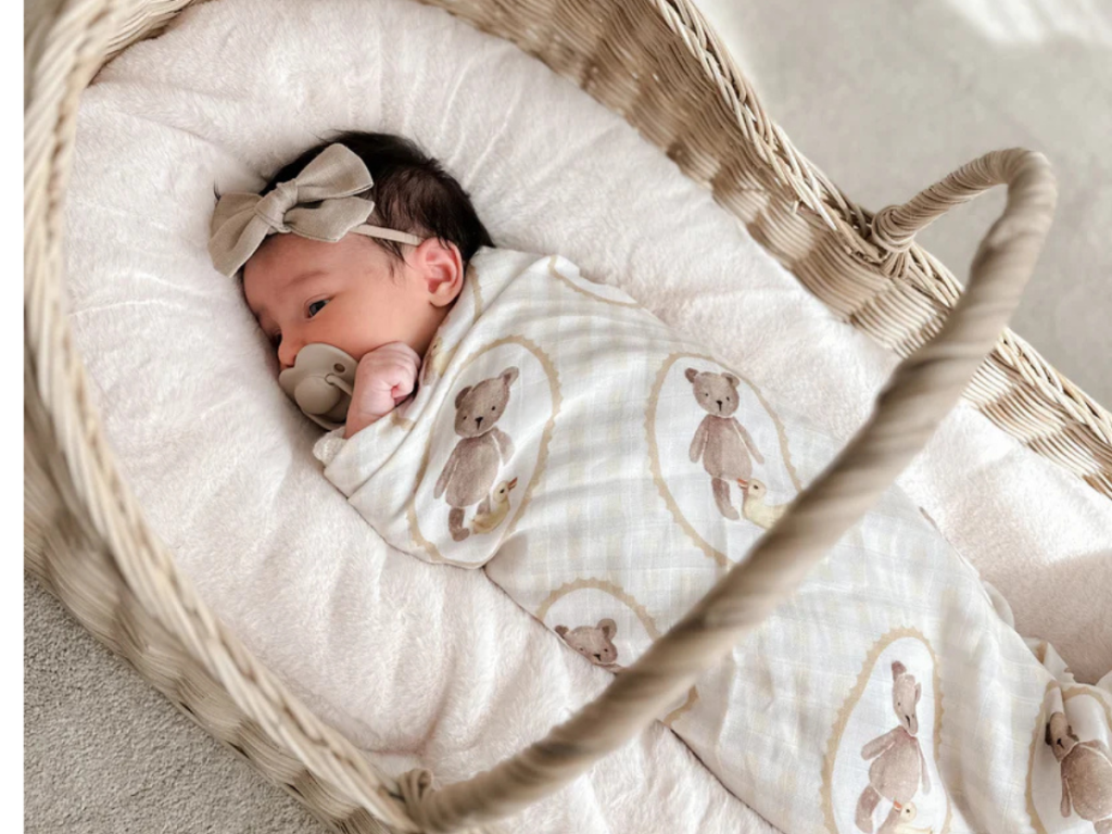 Newborn baby wrapped in teddy bear swaddle in a wicker bassinet.