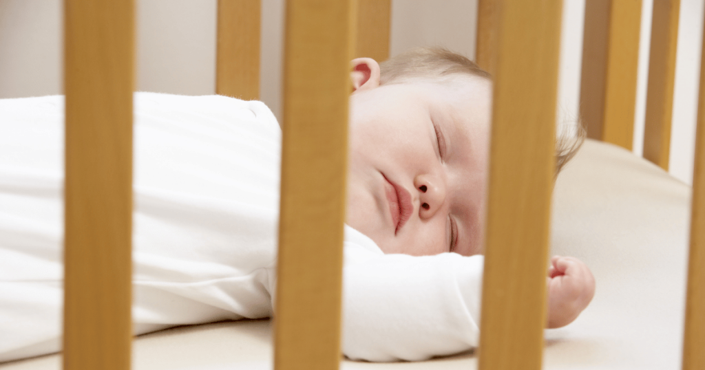 Newborn baby asleep on back in a cot.