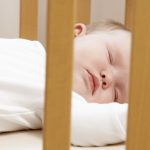 Newborn baby asleep on back in a cot.