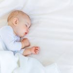 Unsettled newborn sleeping on a white sheet.