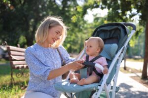 Parent securing baby in a stroller with safety harness outdoors.